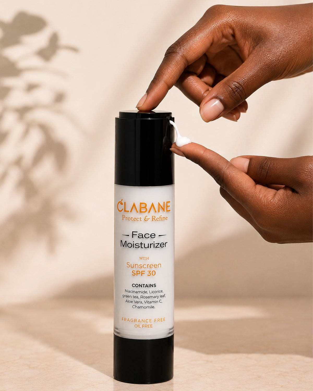 A person's hands are shown dispensing white cream from a black and white bottle of Clabane Face Moisturizer with SPF 30, set against a warm beige background with soft leaf shadows.