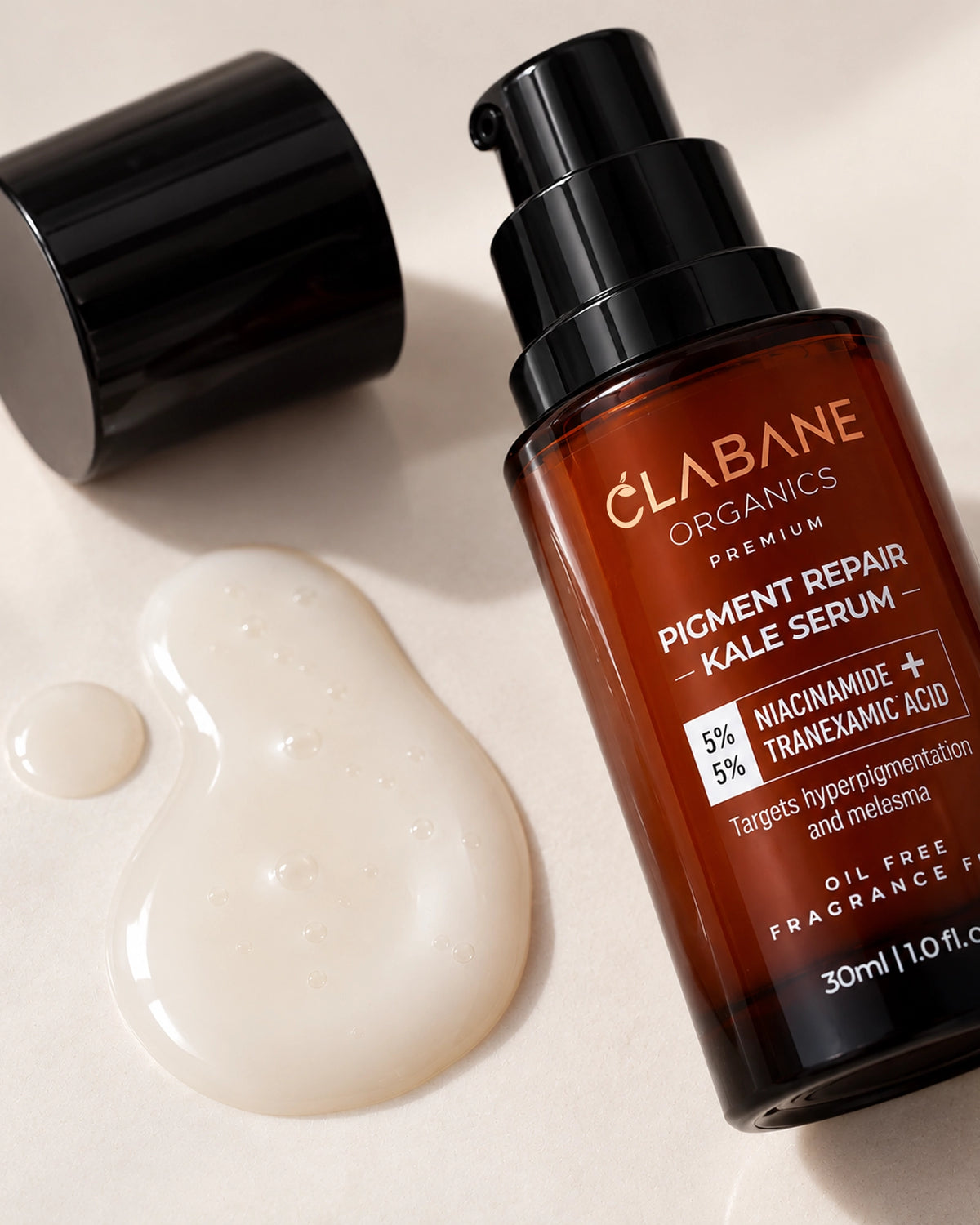A bottle of Clabane Organics Premium Pigment Repair Kale Serum with its black cap off, placed on a light beige surface next to a dollop of white serum.