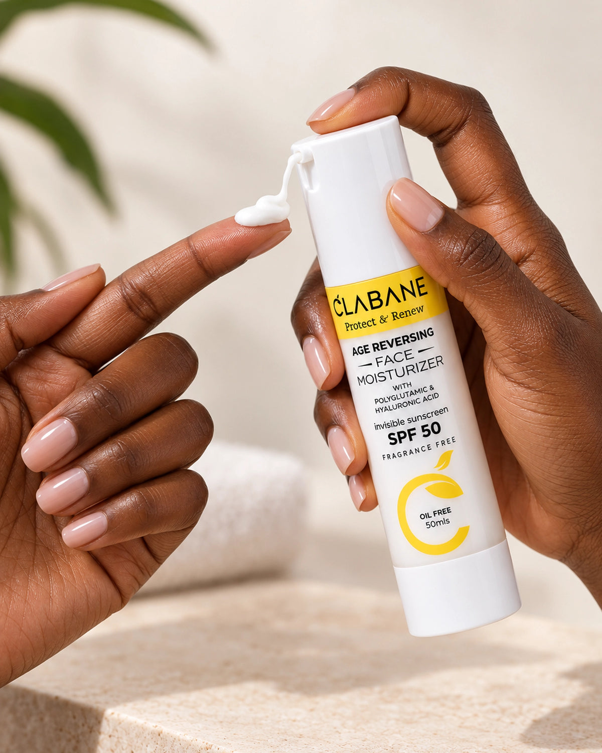 A close-up of a person holding a white Clabane Face Moisturizer SPF 50 tube while applying white cream to their finger. The background is a soft, warm beige with a blurred white towel.