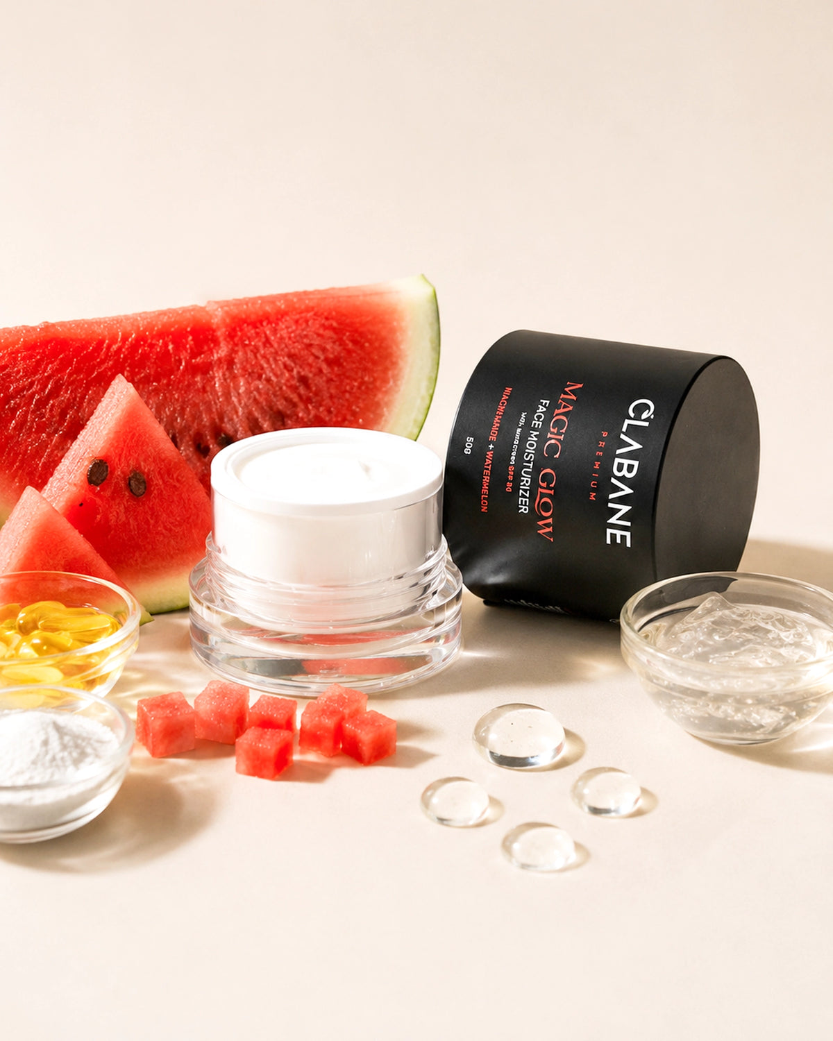 A skincare product set on a warm beige background, featuring a black cylindrical container labeled CLABANE Magic Glow, a white cream jar, clear gel, watermelon slices, and small ingredient bowls.