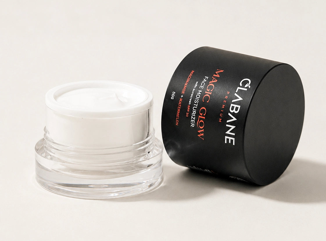 A clear cosmetic jar with a white lid containing white cream, shown beside a black cylindrical box labeled CLABANE MAGIC GLOW AGE MOISTURIZER on a light neutral background.