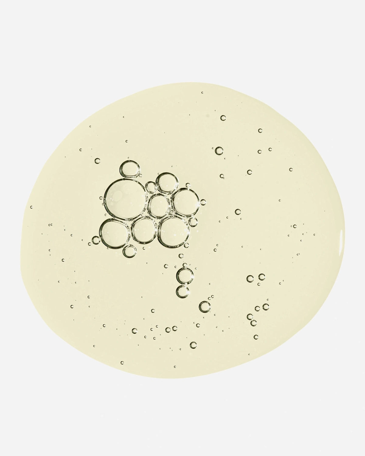A circular swatch of translucent, pale yellow cosmetic gel or serum with embedded air bubbles, shown on a clean white background.